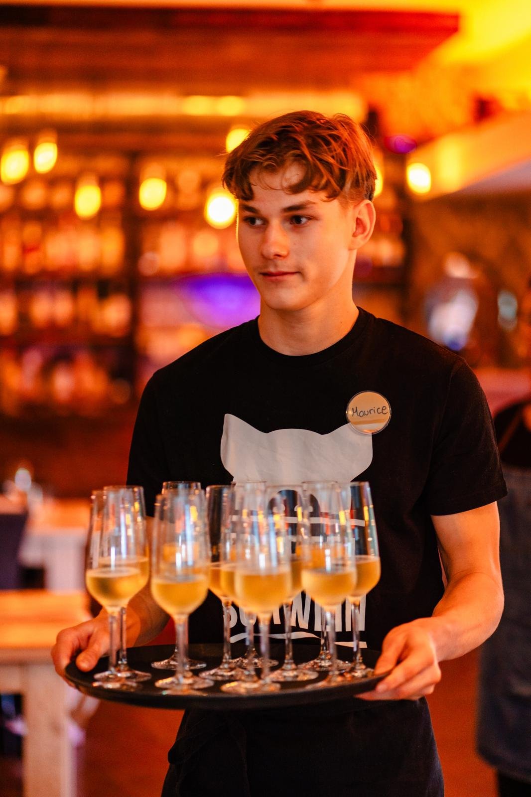 Servicekraft trägt mit ruhiger Professionalität ein Tablett mit Getränken